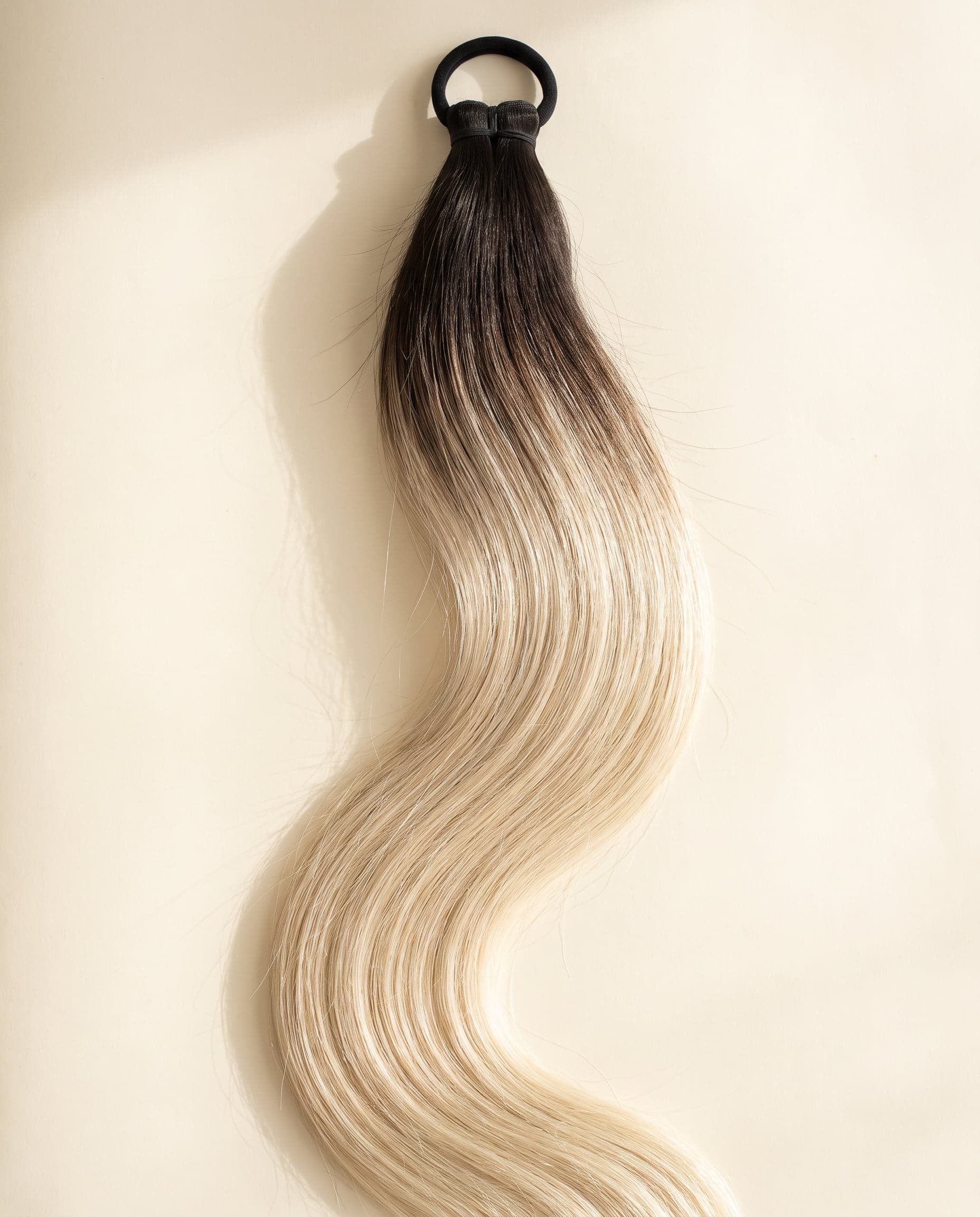 Human hair bundle in color A-2T/613 laid flat on a warm ivory background