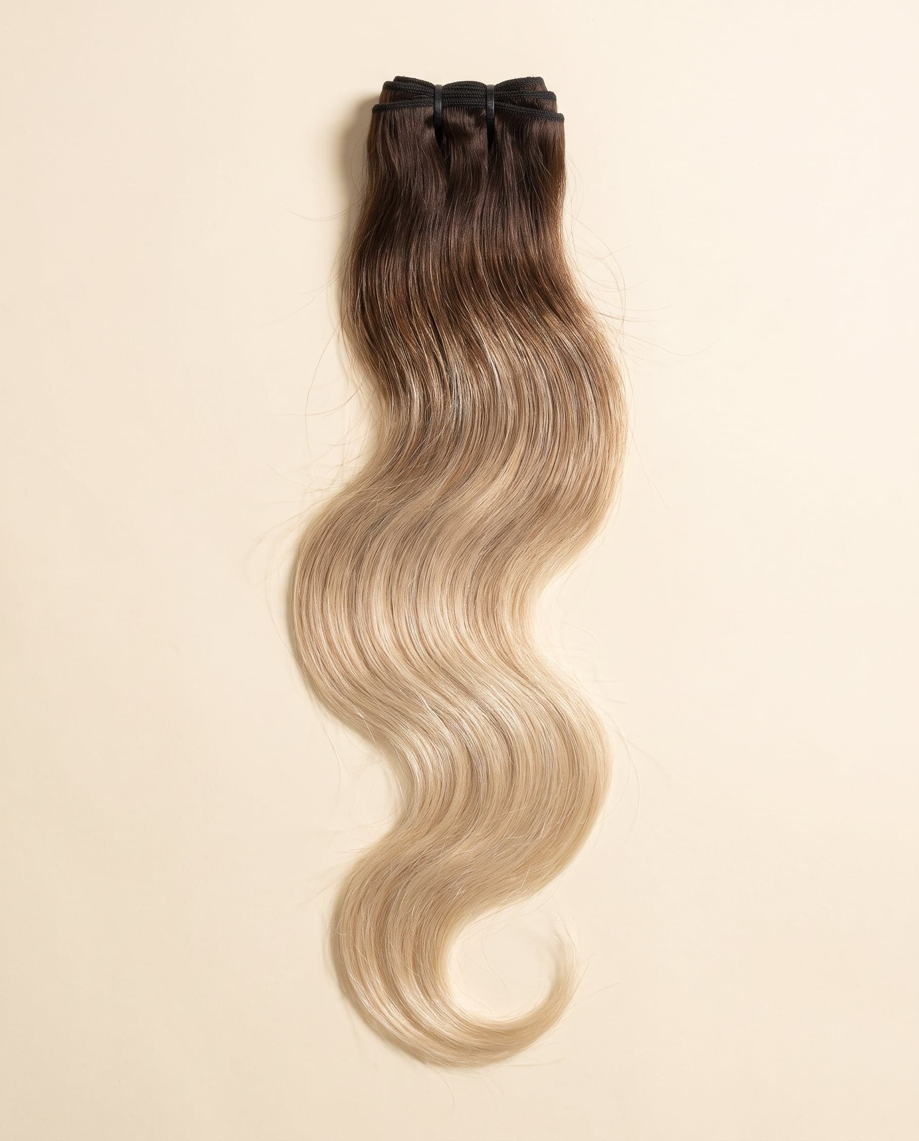 Human hair bundle in color A-3T/613 laid flat on a warm ivory background