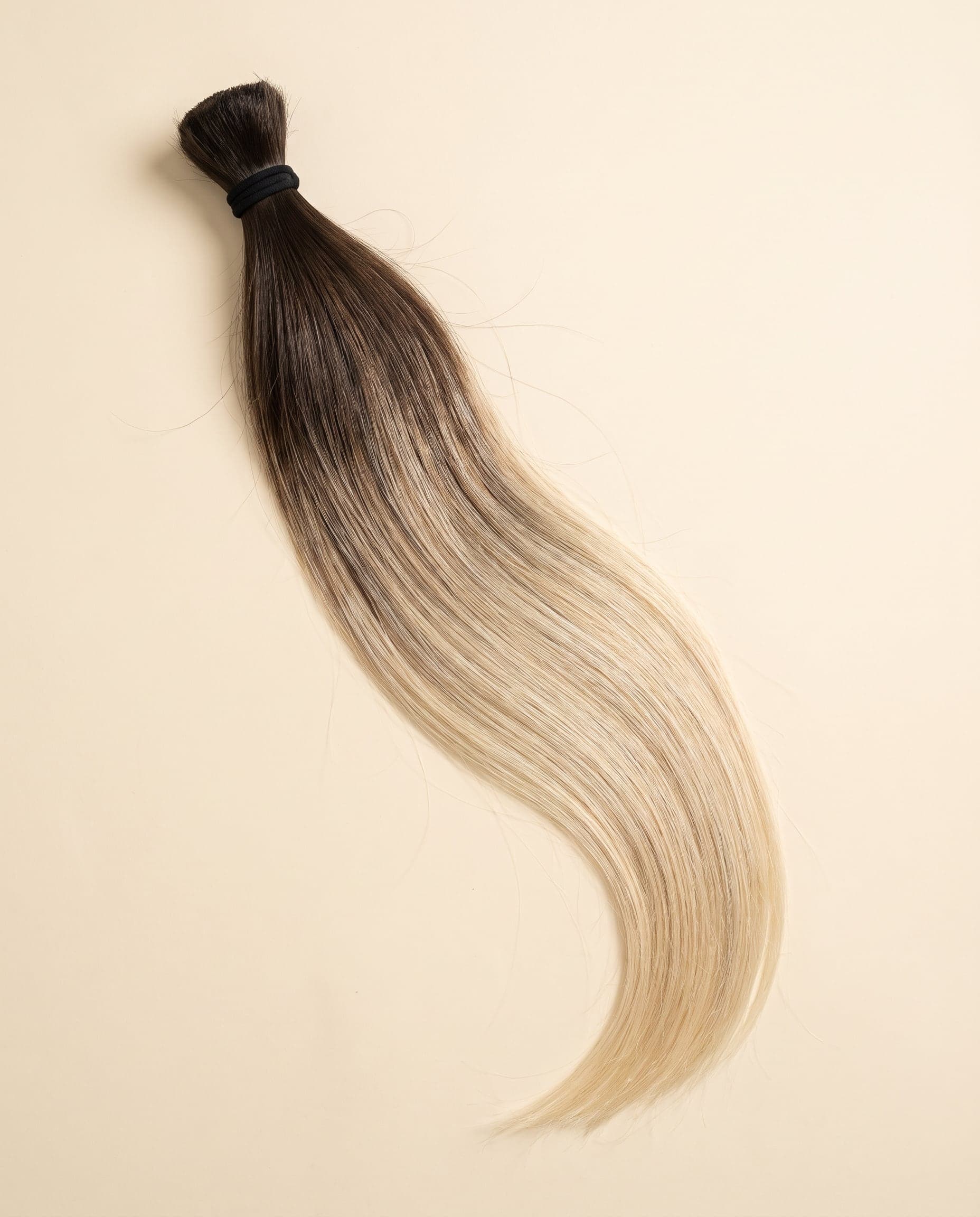 Human hair bundle in color Natural/613 laid flat on a warm ivory background