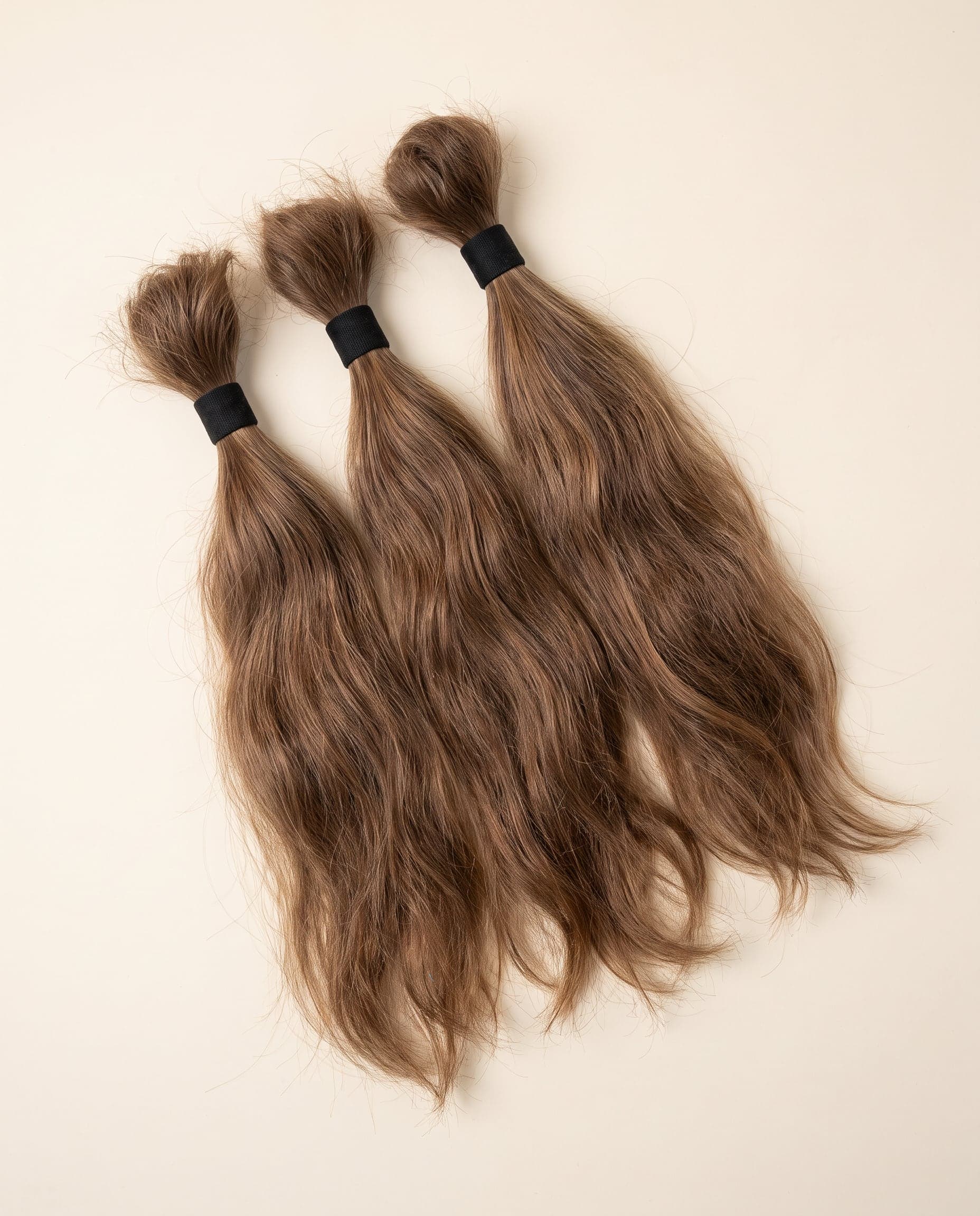 Three Gold grade bundles in warm chestnut brown laid in an overlapping fanned arrangement on a warm ivory surface