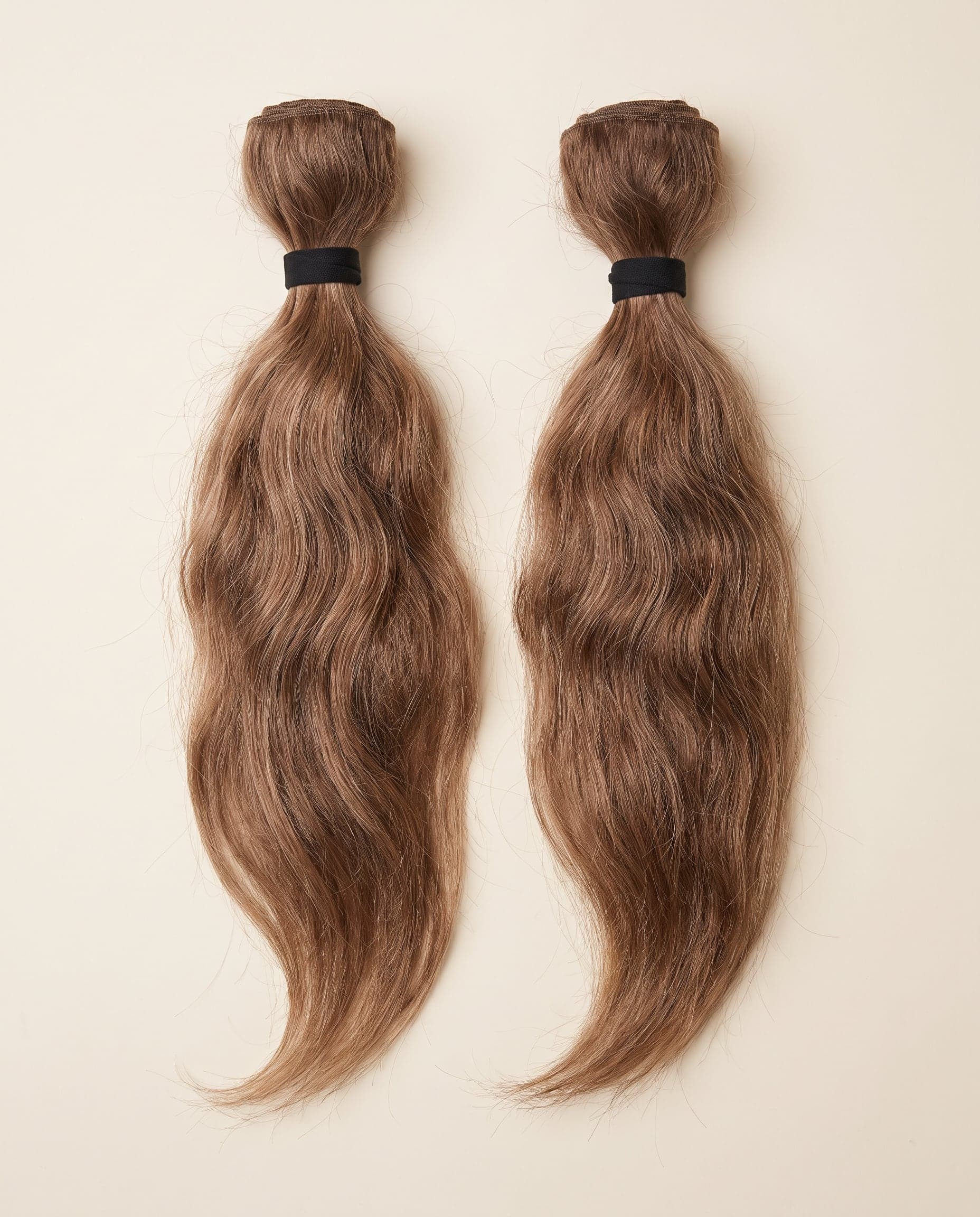 Two Gold grade bundles in natural light brown laid in gentle flowing curves on a warm ivory surface